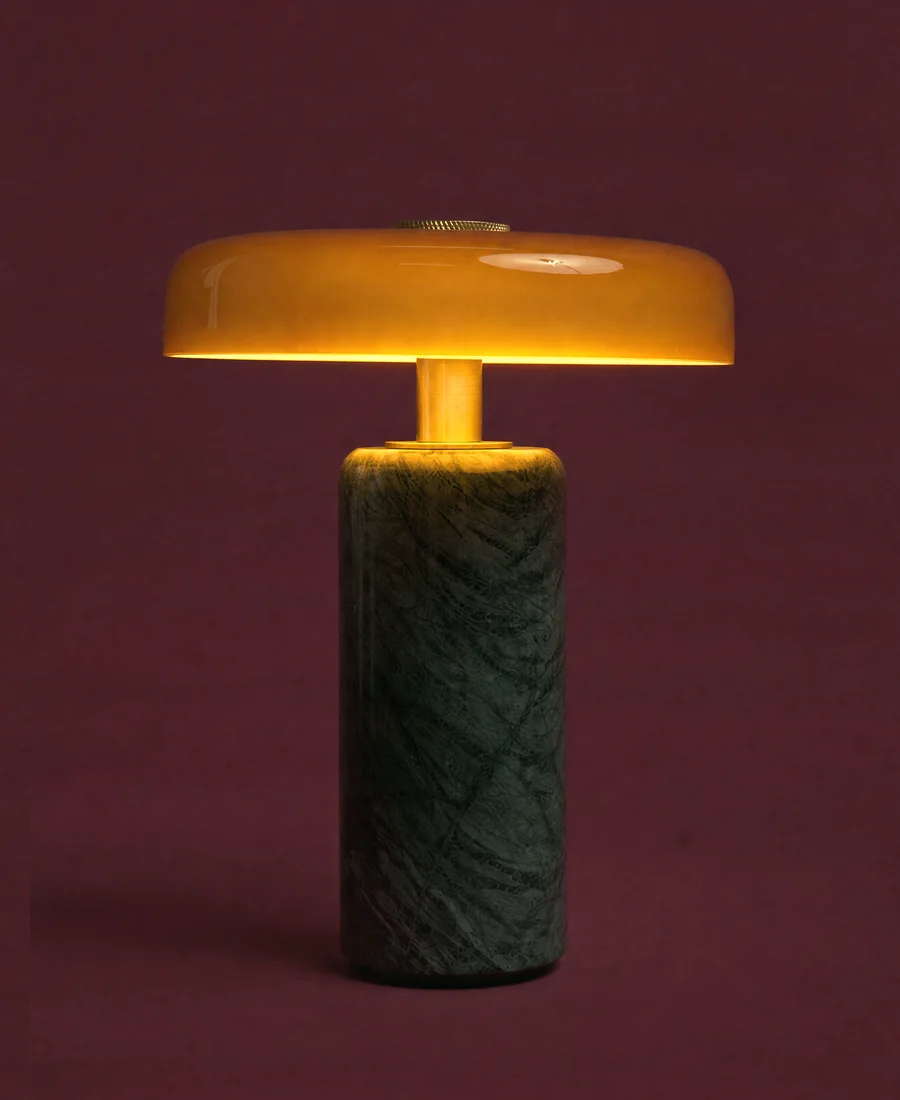 A stone table lamp with an amber glass disc, lit, on an oxblood ground.